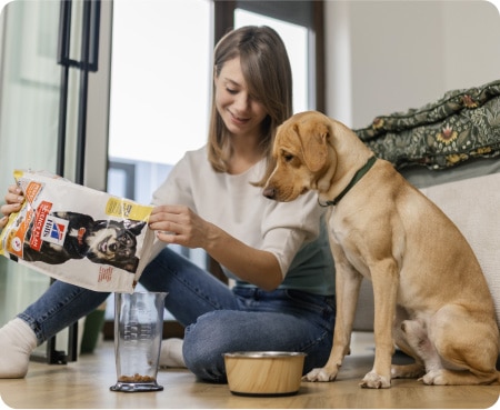 Mujer vertiendo comida de Hill's Pet Nutrition en un recipiente medidor mientras un perro mira atentamente.